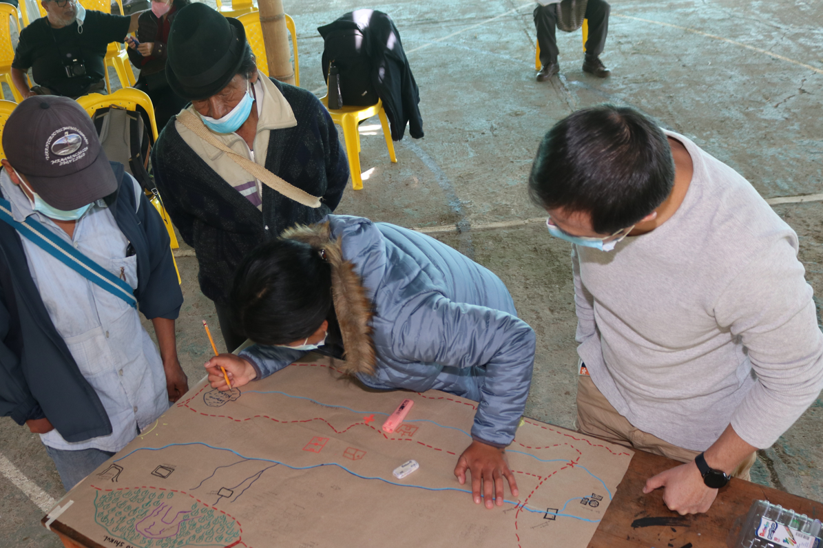 Image shows several participants of the social cartography workshop grouped around a table, where they are adding to a map